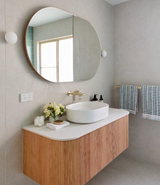 Modern bathroom with round mirror, wooden vanity, and white sink.